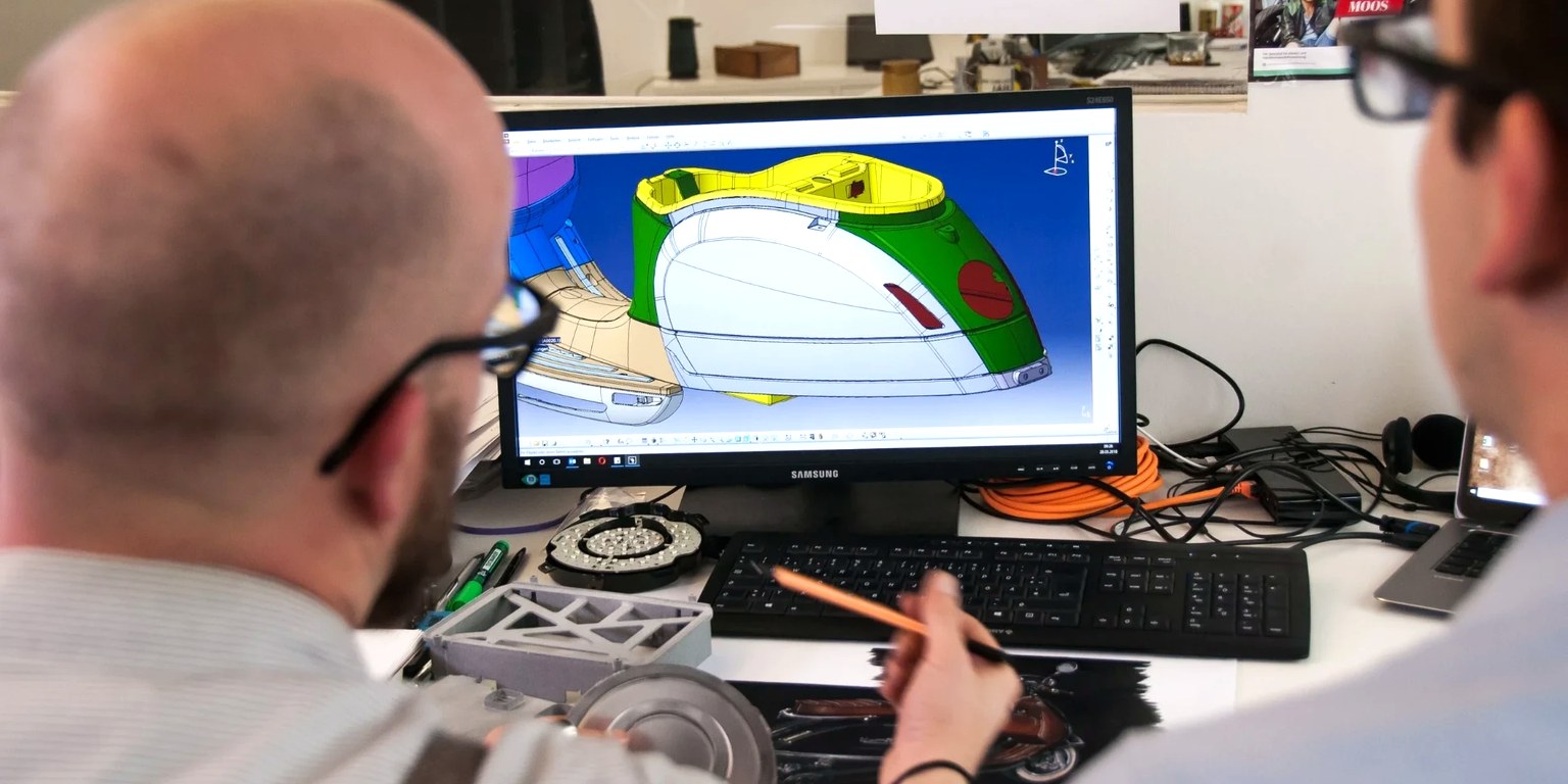 Engineers reviewing a colorful 3D CAD model on a monitor at a workstation
