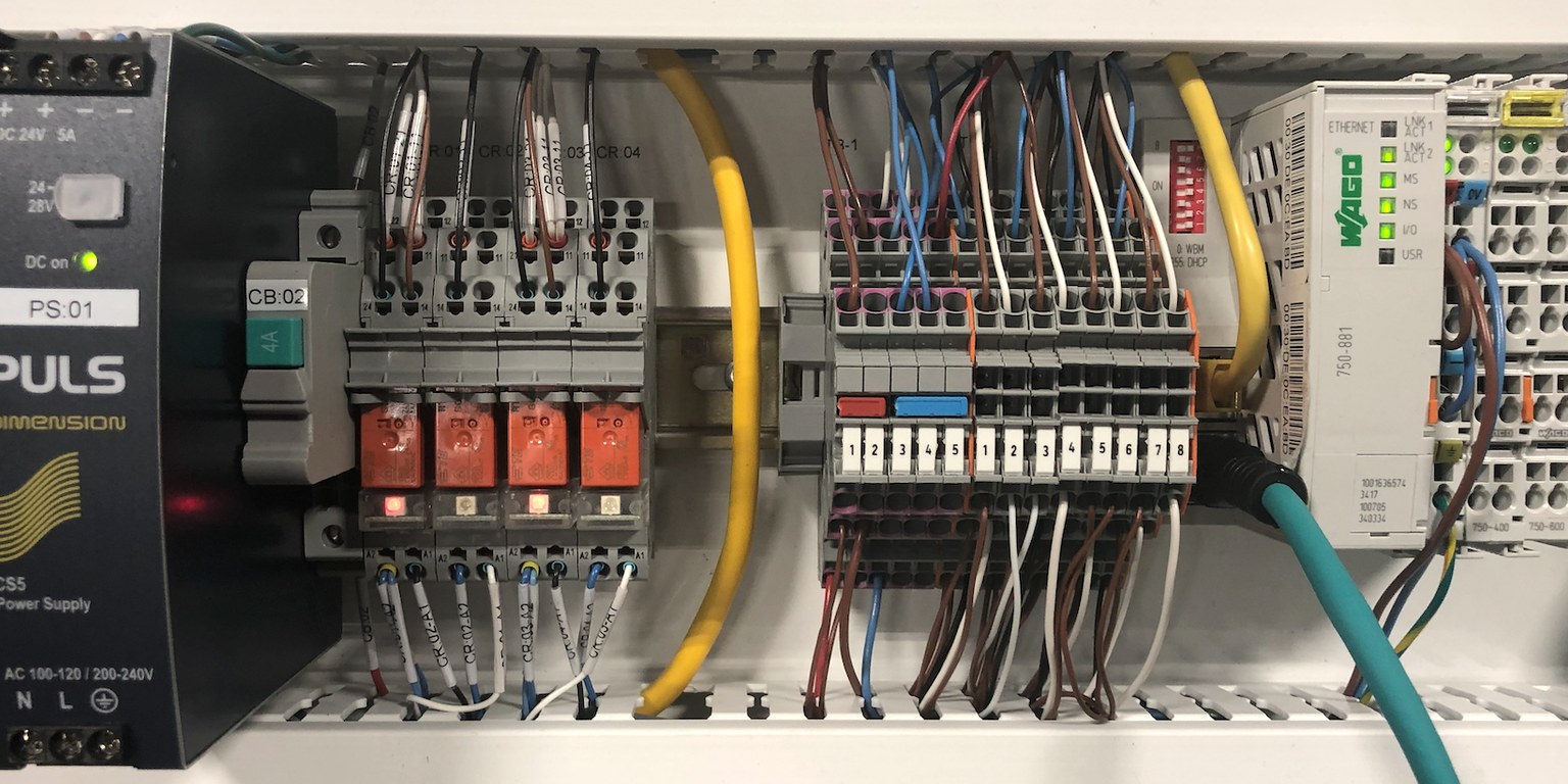 Technician wiring an open industrial control panel with neatly arranged breakers and terminal blocks